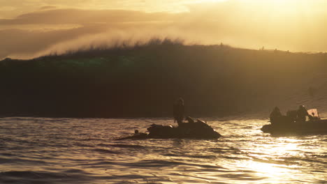 backlit ocean wave crashes as mist spray rises in front of jet ski at sunset