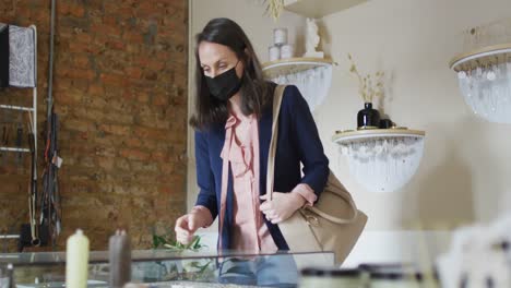 caucasian woman wearing face mask, touching glass surface, shopping for jewelry