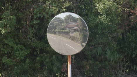 Convex-mirror-reflecting-a-curved-road-and-greenery,-with-clear-sky,-safety-concept