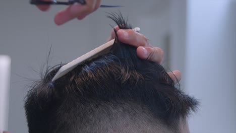 smooth black hair on top of head being measured by hand and comb then cut by scissors, filmed as closeup shot in handheld style on right side of head