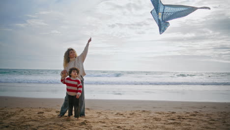 padre niño jugando cometa en la playa del océano fin de semana. joven madre soltera ayudando a su hijo