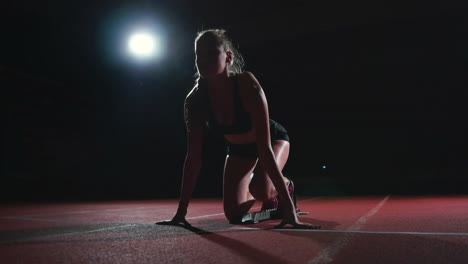 slender young girl in track and field is getting ready to start in the race in the running pads on a black background