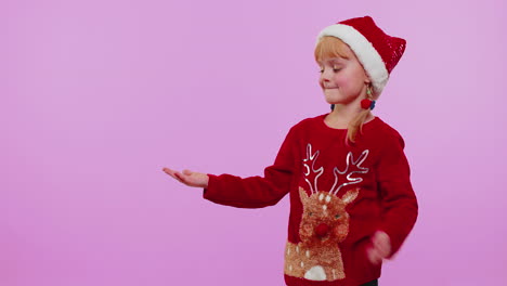 Girl-child-in-Christmas-sweater-deer-showing-thumbs-up-and-pointing-at-on-blank-advertisement-space