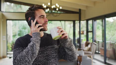 caucasian man talking on smartphone and drinking coffee in dining room