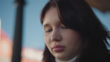 close-up of young woman with pink lips, slightly downcast eyes, and nose ring, focusing with thoughtful expression, soft lighting, calm and serene look, with blurred background