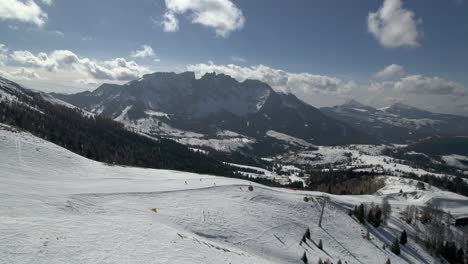 Drone-shot-showcases-Carezza-Ski-Resort,-featuring-the-Konig-Laurin-lift,-a-slope-with-skiers,-and-the-majestic-backdrop-of-the-Latemar-mountain-range-in-the-background