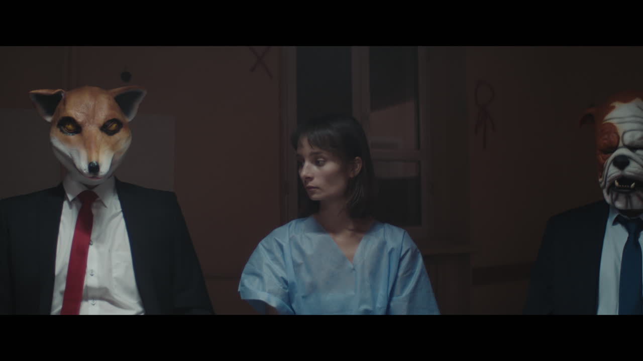 A girl sits at a table with strange figures in animal masks