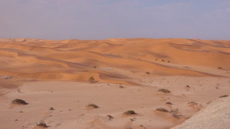 Toma-Panorámica-A-Través-De-Vastas-Dunas-De-Arena-Del-Desierto-De-Namib,-Namibia-A-Una-Mujer-Sentada-En-Un-Balcón-De-Un-Resort-Lodge