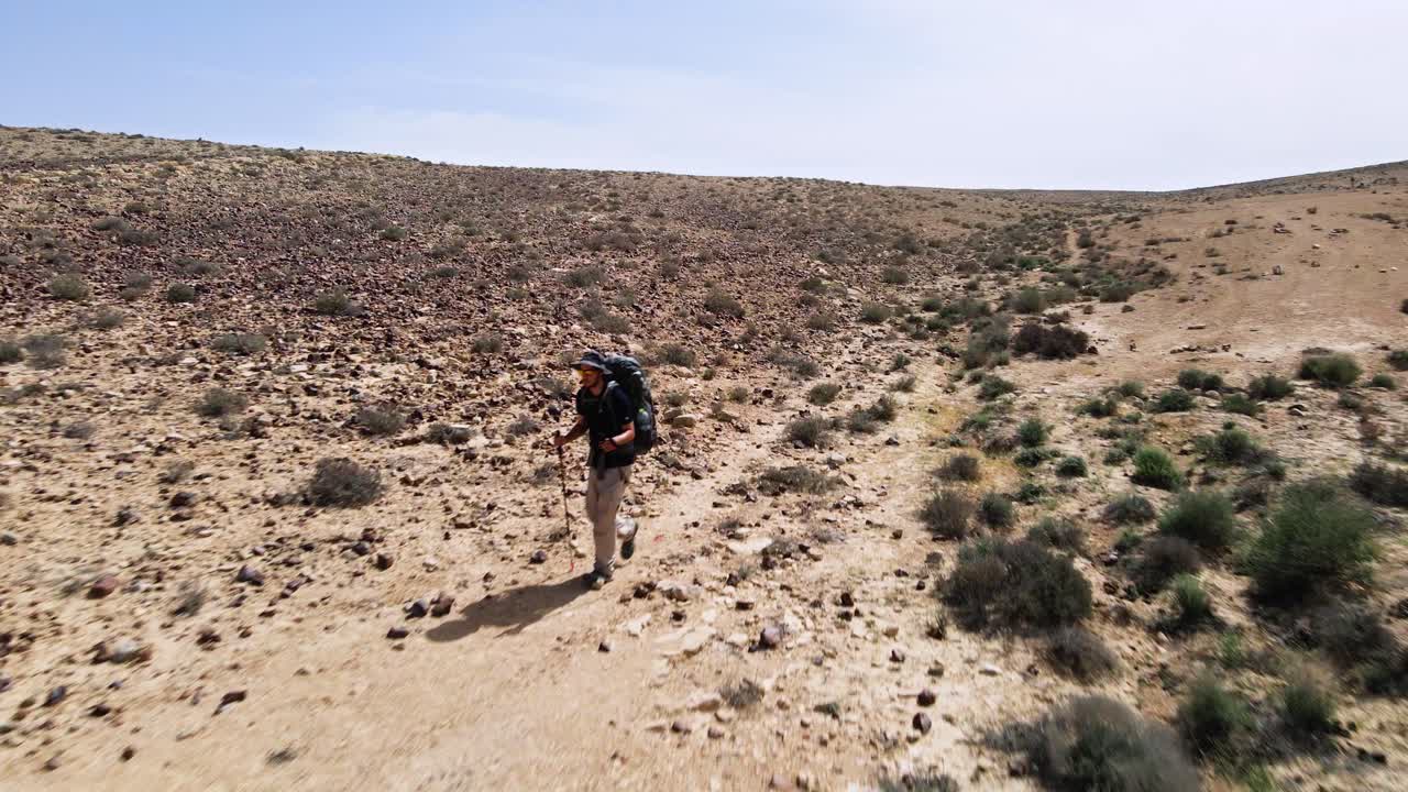 Fast drone fly in towards hiker walking a track in rocky desert wilderness landscape