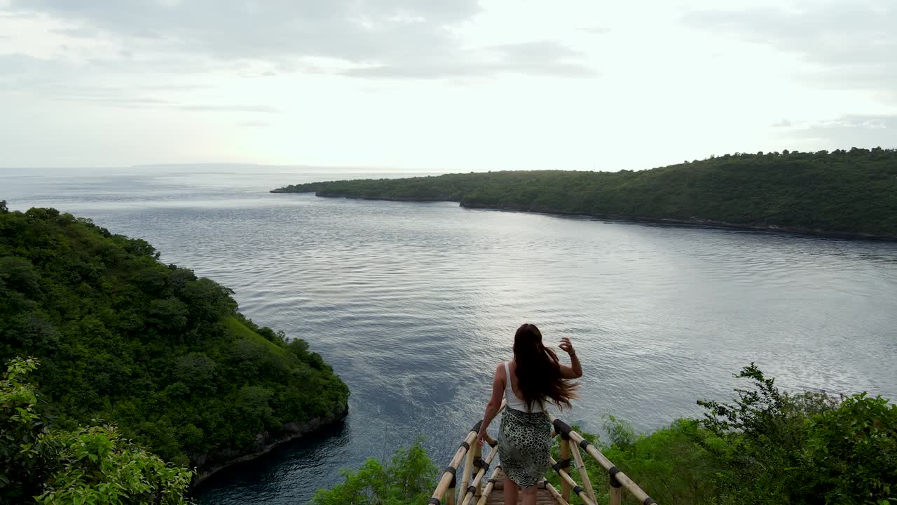 mujer viajera caminando al borde de la plataforma de madera con vistas a la bahía al atardecer