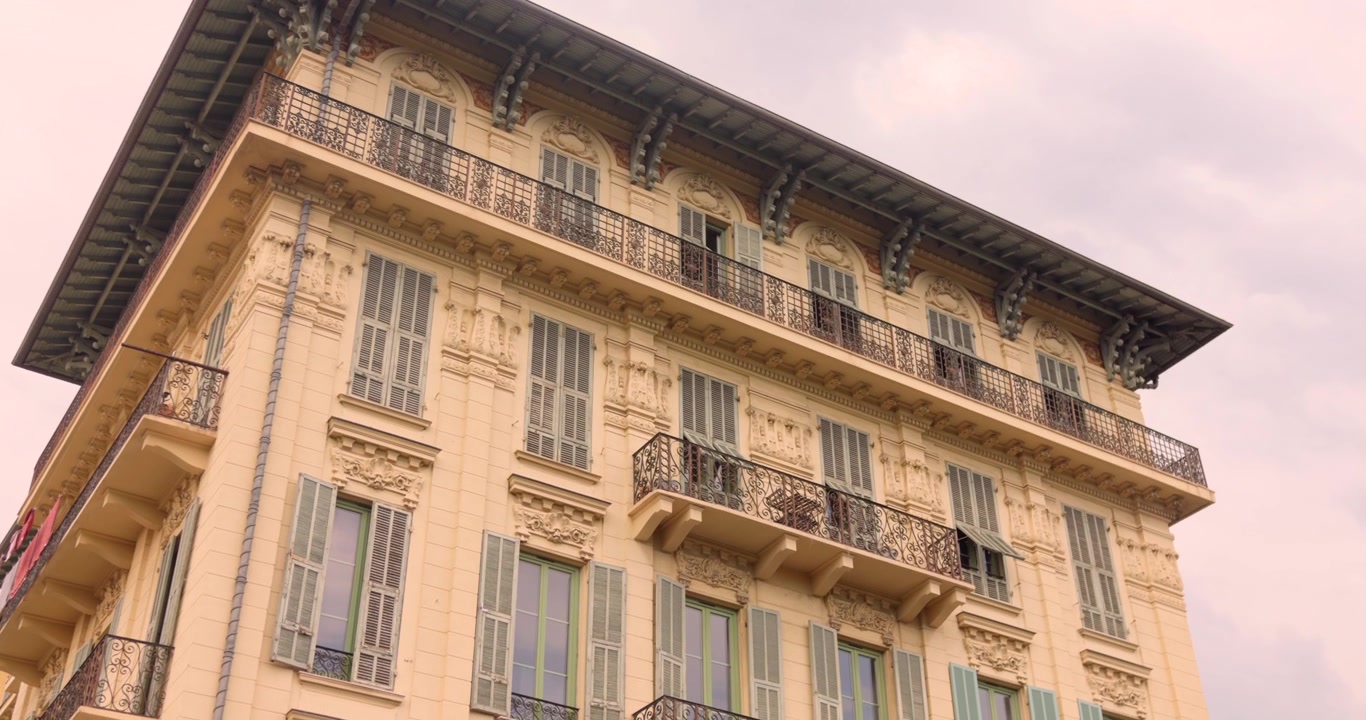 Palazzo storico ornato a Nizza con finestre alte e balconi in ferro battuto, incorniciato contro un cielo nuvoloso.