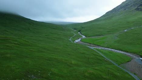 Drone-shot-revealing-green-country-road-under-mountain