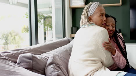 happy african american senior mother and adult daughter sitting on couch and embracing, slow motion