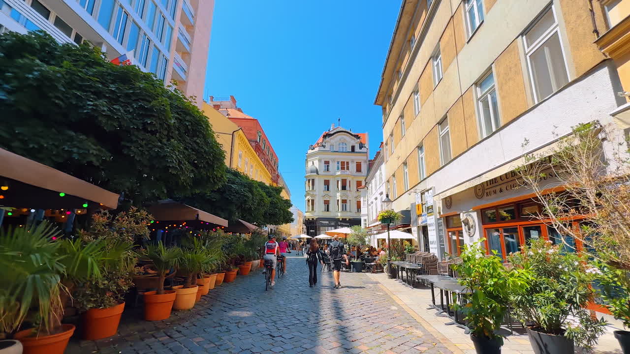 Bratislava, Slovakia, 2 June 2025: Exploring a vibrant street in Bratislava. People walk along a vibrant cobblestone street in Bratislava, with cafes and greenery under a clear blue sky