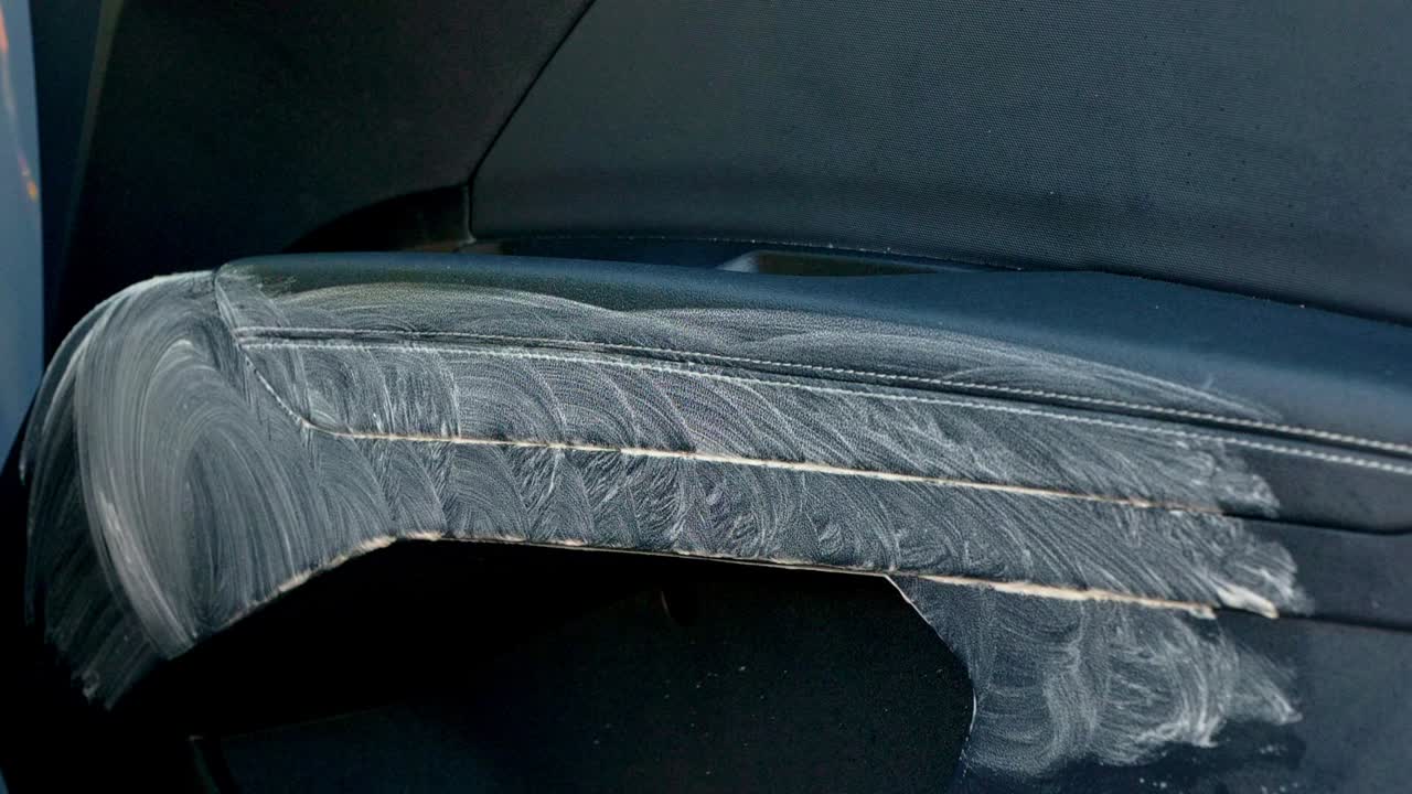 Wiping away cleaning product from car leather interior door arm rest with yellow microfibre towel