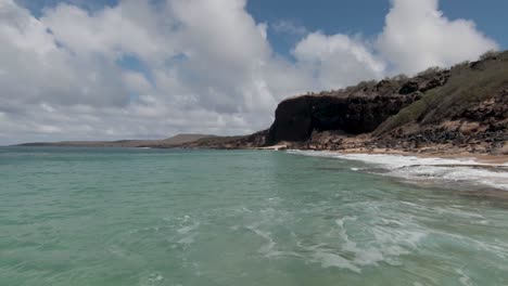 epic speed flying fpv racing drone over green ocean with some mountains and cliffs in background - cinematic drone footage