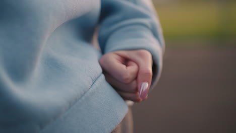 close up of lady with polished nails brought closely to waist making hand gesture with blurred background, soft lighting highlights her cyan sweater and athletic posture during exercise