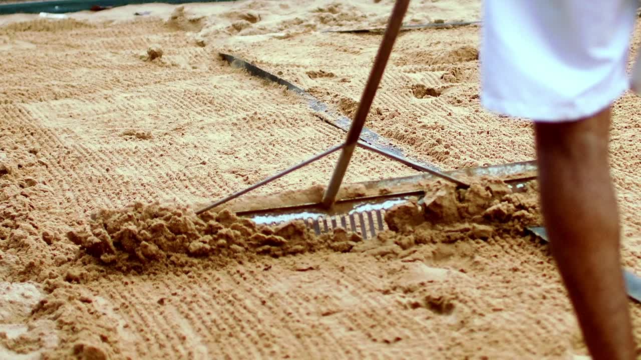 해변 테니스 코트 주위 에 모래 를 옮기기 위해 나무 로 된 래크 를 사용하는 공무원