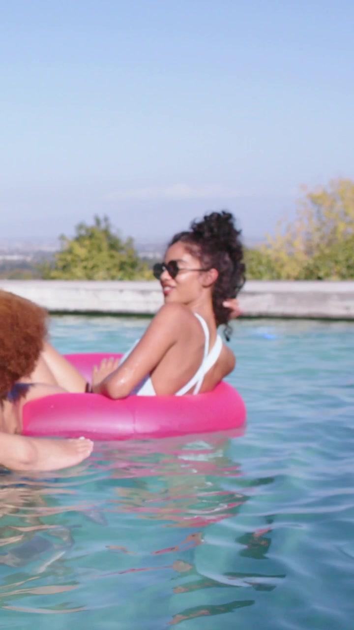 Vertical video: White-swimsuit woman turning as pal climbing onto pink ring at home pool, relaxing