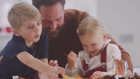 father with children at home doing craft and making picture from leaves in kitchen