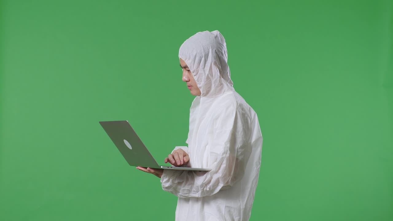 아시아 남성 과학자가 녹색 화면 배경에서 노트북에서 타이핑하고 있습니다.