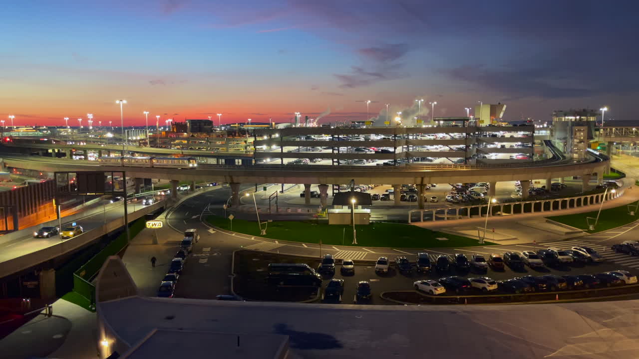 에어트레인 jfk는 하늘이 석양에 물들 때 뉴욕 공항의 주차장을 지나 도로에서 고가 철도를 여행합니다.