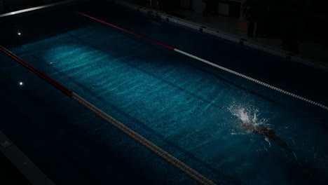 a swimmer in a red swim cap doing freestyle in a pool at night