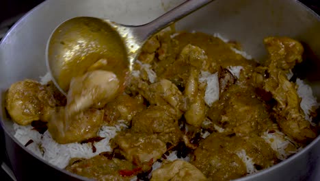 fresh curry chicken being placed on top of white rice in large pot