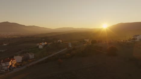 golden sunset over a small mountain village with scattered houses, rolling hills, and distant peaks. greece
