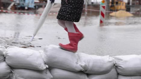 Kleines-Mädchen-Läuft-Auf-Dem-Stapel-Sandsäcke-Wegen-Überschwemmung-Auf-Der-Straße