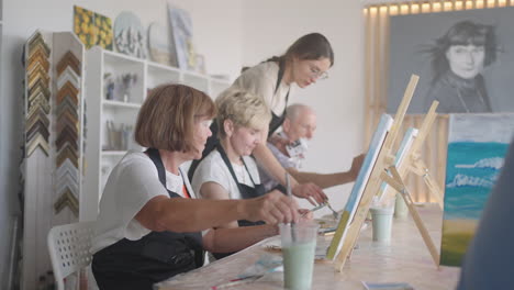 high angle view of cheerful senior friends painting on canvas. senior woman smiling while drawing with the group. seniors attending painting class together. senior men having fun painting in art class