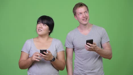 young happy multi-ethnic couple using phone and thinking together
