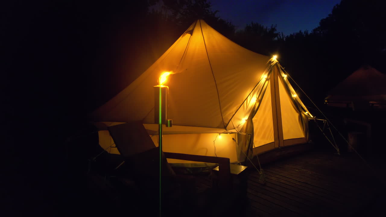Tenda con torcia accesa, lampade e sedie di legno in un glamping, di notte