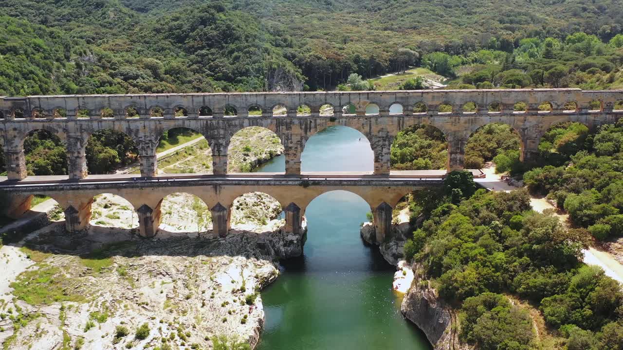 Tilted Aerial View of the Pont du Gard Aqueduct over the H&eacute;rault River, with a Canoe in the Background on a Summer Day in Occitanie