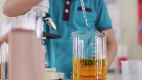 niño con máscara facial y gafas protectoras usando pipeta y vasos en el laboratorio