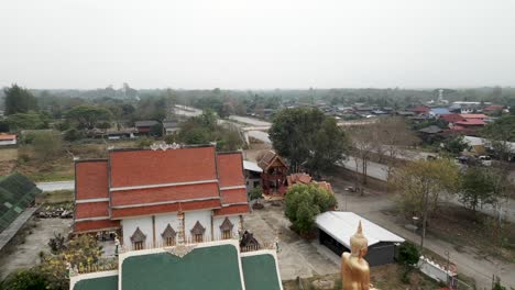 aerial view of a buddhist temple complex with a golden buddha statue in a thai village