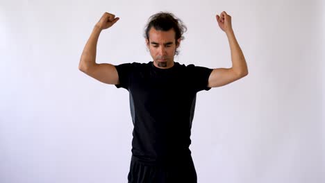 un hombre hispano de pelo largo con perilla realiza un estiramiento activo de la muñeca frente al fondo blanco del estudio