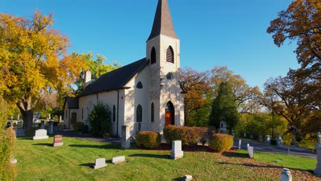 low flying drone over rural cemetery with smal country church and autumn trees