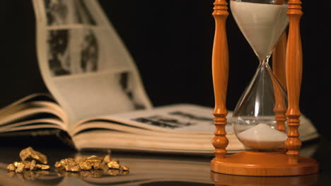 pages turning in the wind beside hourglass and gold nuggets