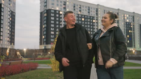 playfully cheerful lady tickles her brother ear while walking together in modern urban park, he smiles warmly trying to resist while telling her to stop as both share light-hearted bonding moment
