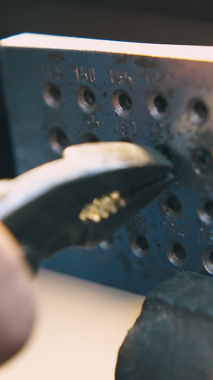 CU: professional jeweler pulls white gold rod through hole of metal tool die with pliers at workplace close view