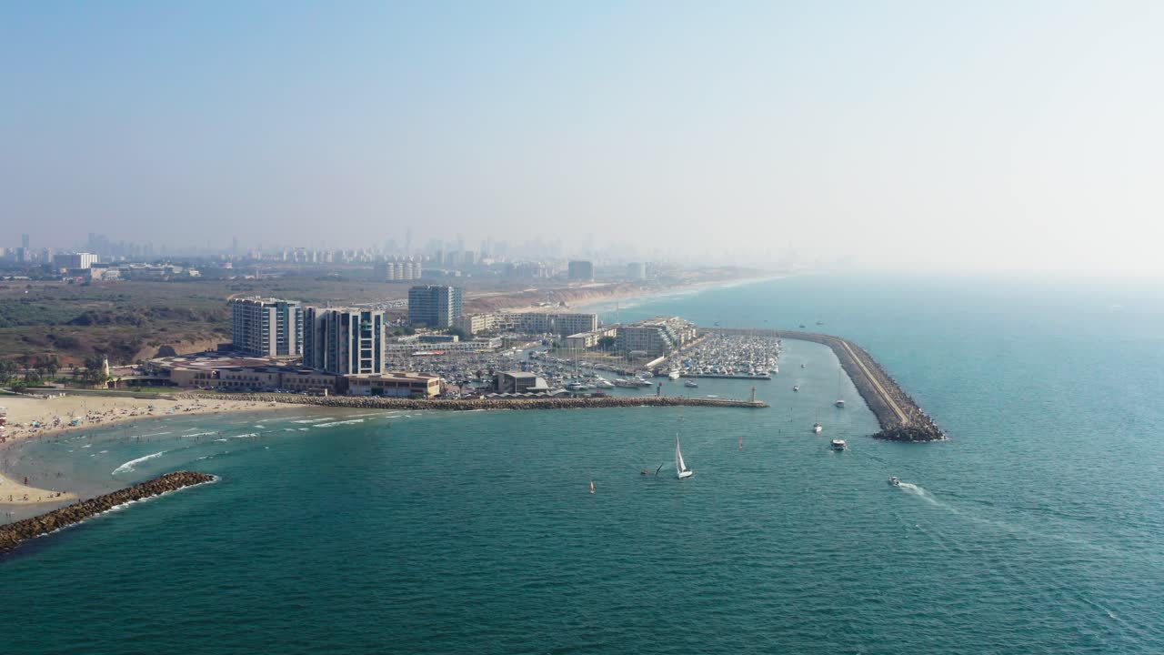 Beautiful coastline of vast sandy beaches and the large Herzeliya Marina where several sailing yachts and motorboats navigate from the clear Mediterranean Sea in Israel. Aerial drone dolly shot