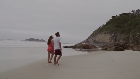 Couple Walking on a Sandy Beach with Waves and Coastal Cliffs