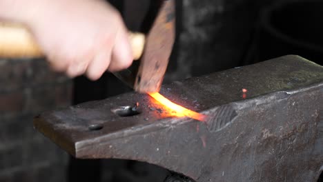 blacksmith stokes a coal fire and pounds a red hot peice of metal with a hammer