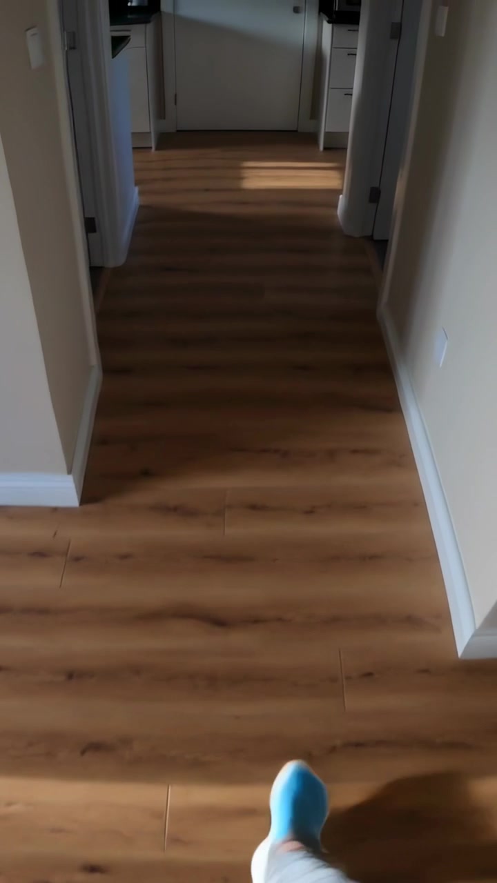Vertical video: Walking blue-socked foot moving down wood hall toward closed door, camera starting