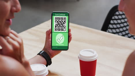 hombre en un café mostrando un teléfono inteligente con certificado de vacunación contra la covid y código qr en la pantalla