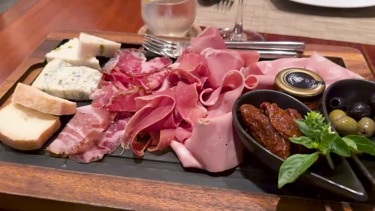 Ripresa panoramica ravvicinata di un tagliere di legno con prosciutto, salame, mortadella e formaggio erborinato