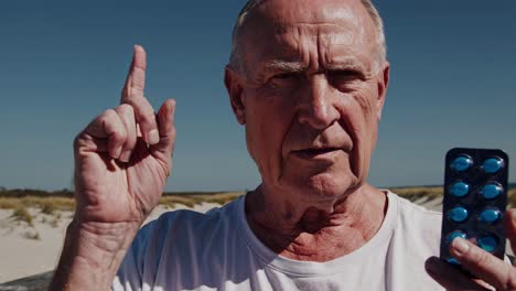 elderly man holding pills on a beach