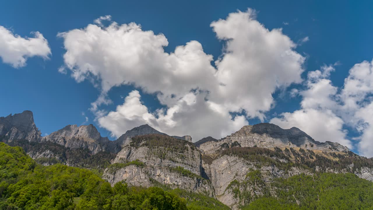 Timelapse on a spring day. Clouds swirl above the Churfirsten massif. Nature blooms, and the sun illuminates the landscape. The play of shadows can be seen on the mountain peaks. A natural spectacle.