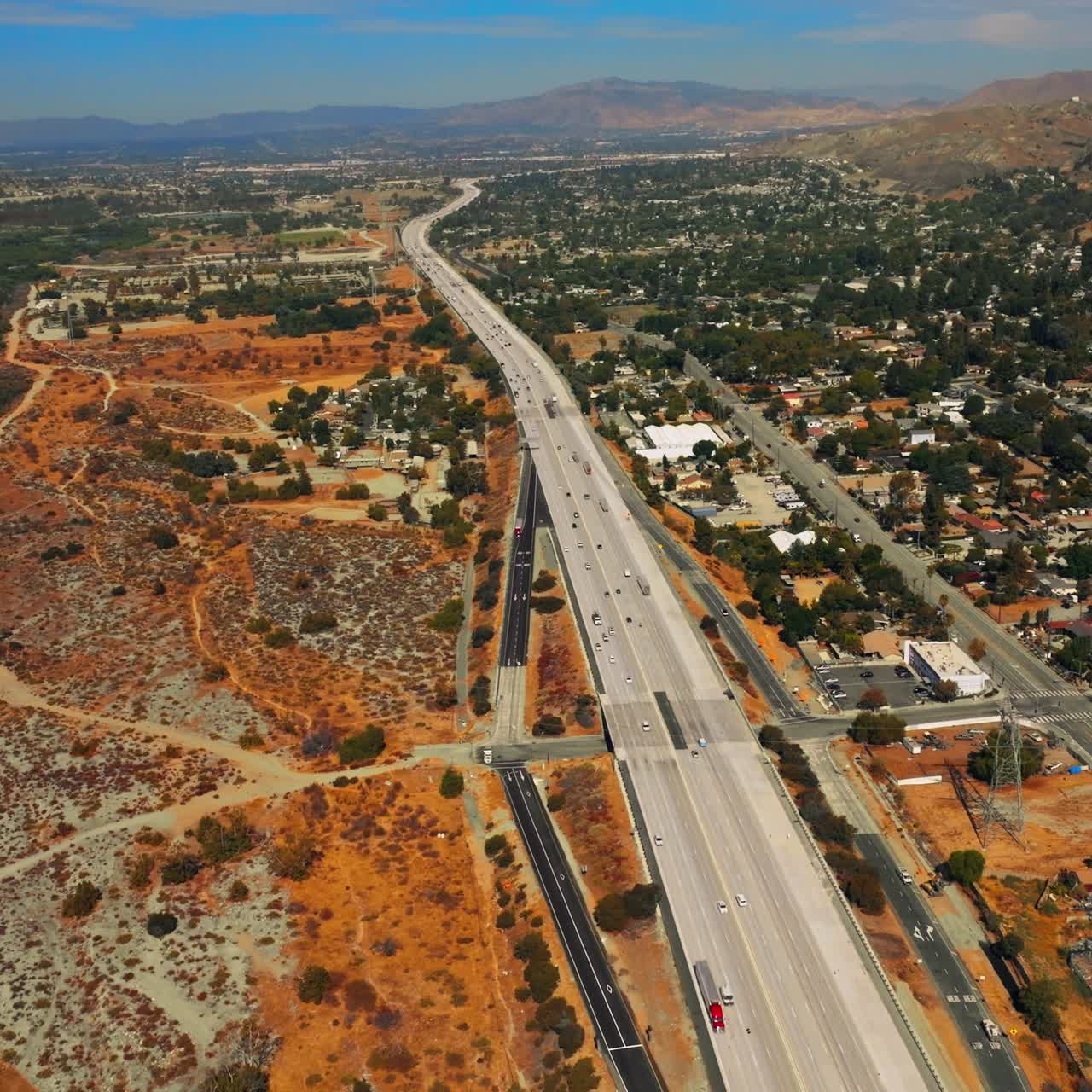 Dry landscape of Los Angeles outskirts on hot sunny daytime. Roads going through sandy lands. Mountain at backdrop